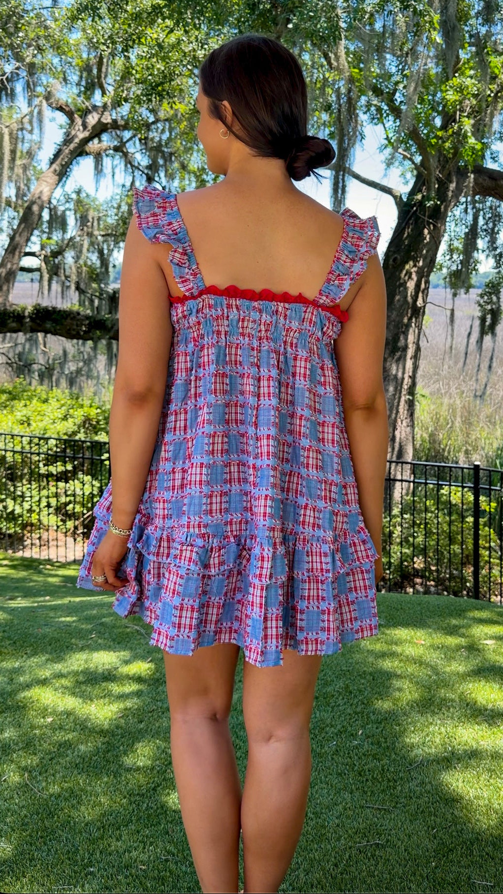 Woman wearing a blue plaid dress with red trim in a park setting