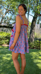 Woman in a plaid dress standing in a park with trees and grass.