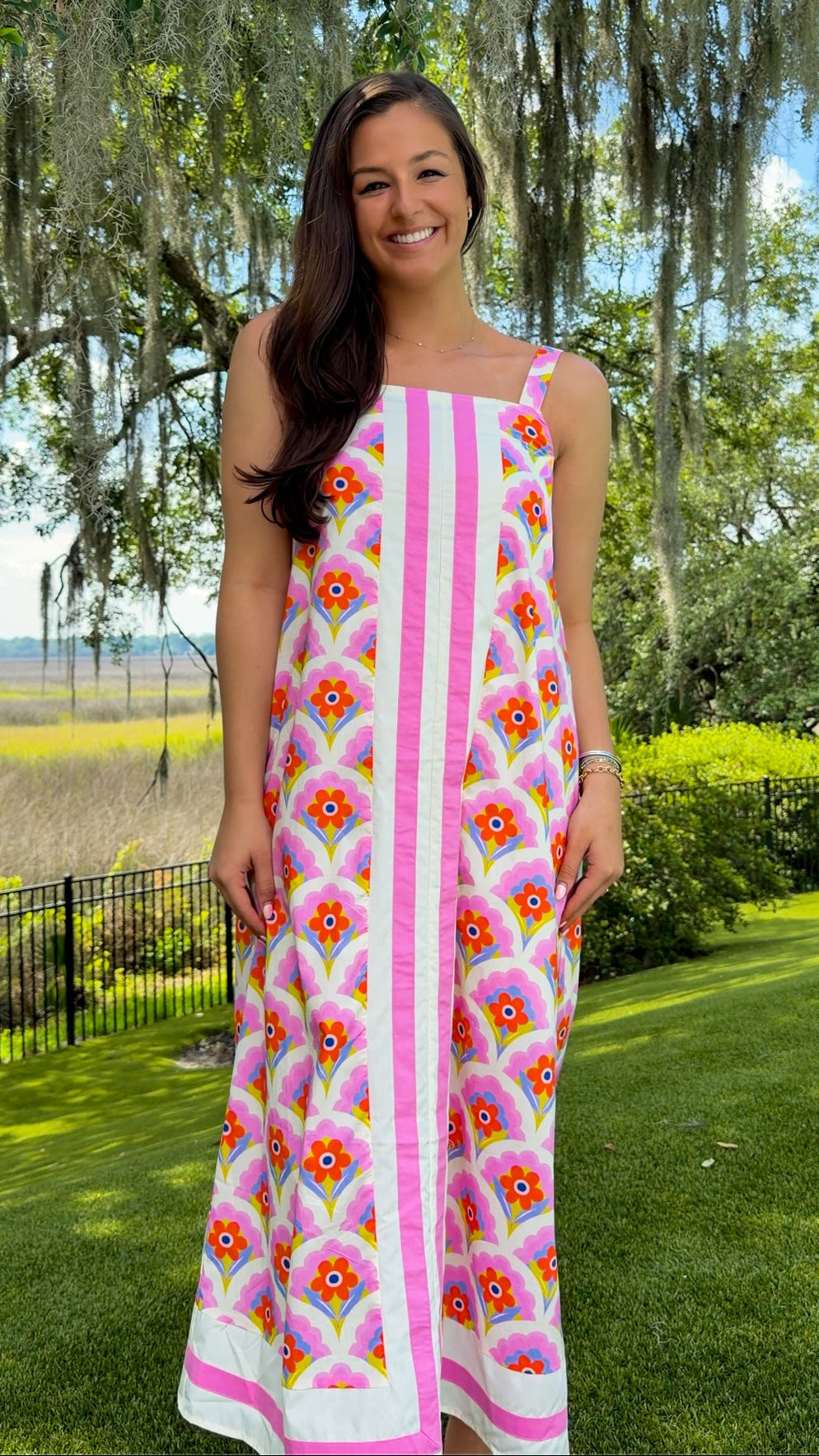 Woman in a floral dress standing outdoors with trees and grass in the background