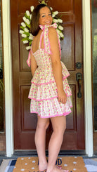 Pastel pink floral tiered mini dress with a smocked bodice, adjustable shoulder tie straps, lace trim detailing, and a flowy tiered skirt.