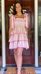 Pastel pink floral tiered mini dress with a smocked bodice, adjustable shoulder tie straps, lace trim detailing, and a flowy tiered skirt.