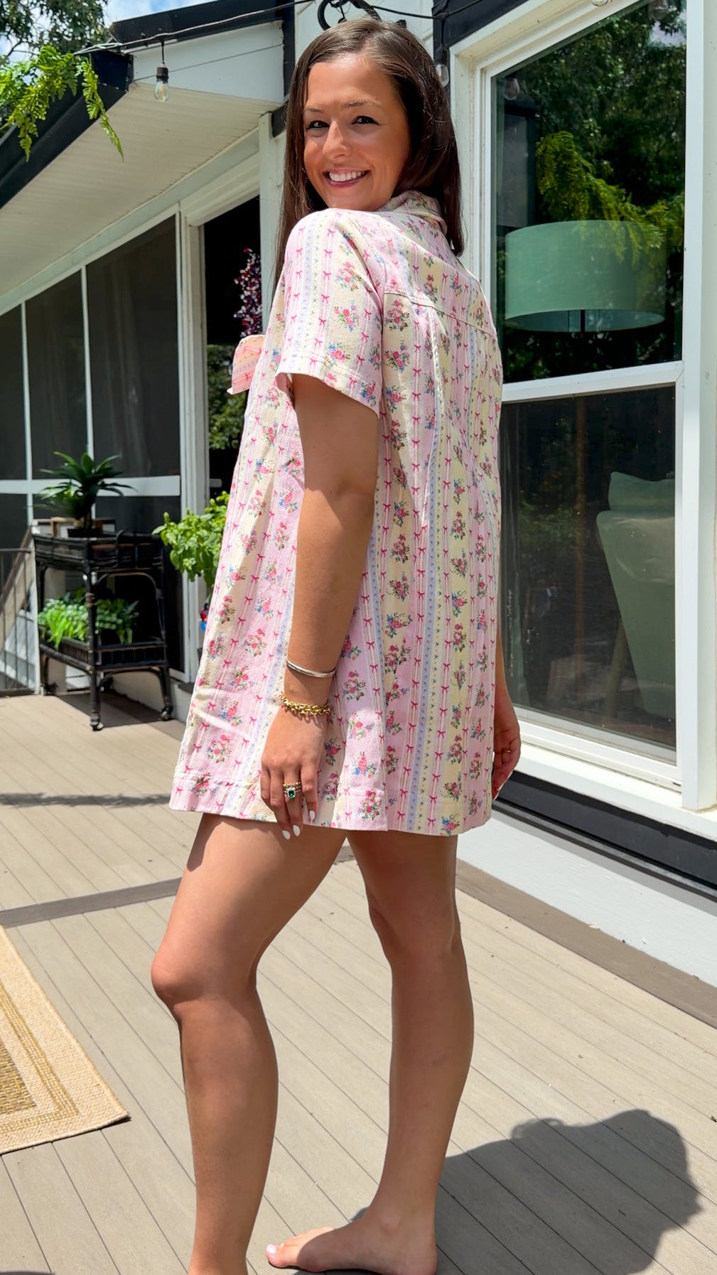 Light pink floral stripe mini dress with a collared neckline, front button closure, short sleeves, oversized bow detail, and relaxed A-line silhouette.