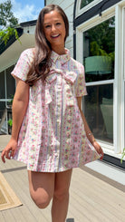 Light pink floral stripe mini dress with a collared neckline, front button closure, short sleeves, oversized bow detail, and relaxed A-line silhouette.