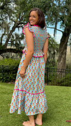 Light blue floral print midi dress featuring a fully smocked bodice, flutter sleeves with pink contrast trim, a keyhole tie neckline, ruffled peplum waist, tiered midi skirt, and side pockets.