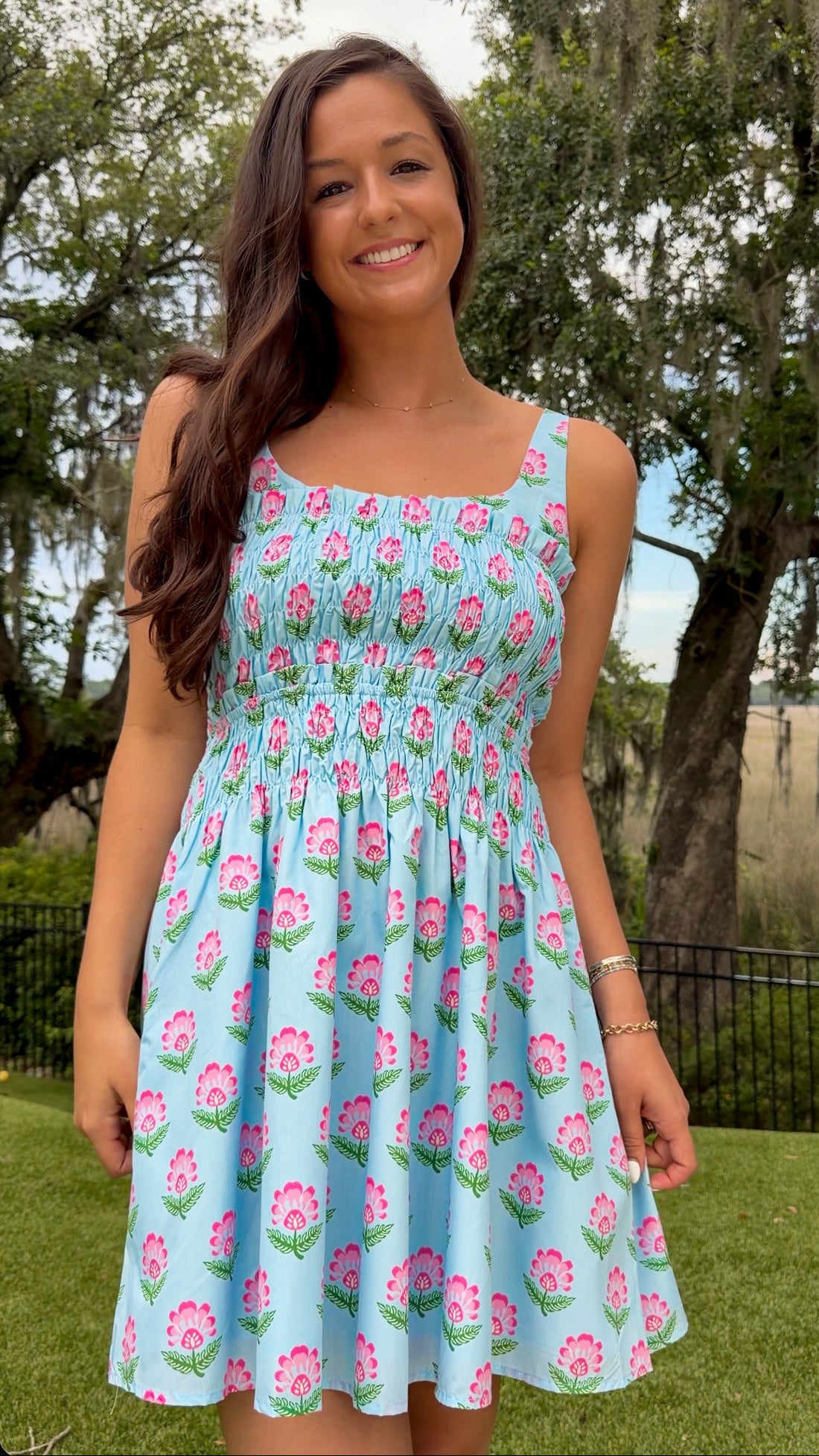 Light blue floral print mini dress featuring a softly scooped neckline, wide shoulder straps, a fully smocked bodice, side pockets, and a flowy flared skirt.