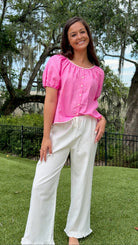 White full-length straight-leg pants featuring an elastic drawstring waistband, side and back patch pockets, delicate ruffle trim at the hem, and a relaxed, lightweight fit.