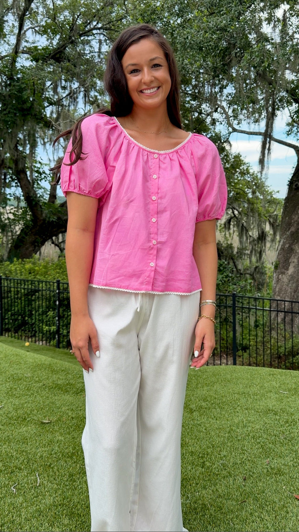 Pink lightweight woven top featuring a gathered scoop neckline with delicate white lace trim, functional front buttons, short puff sleeves, and a relaxed silhouette.