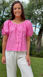 Pink lightweight woven top featuring a gathered scoop neckline with delicate white lace trim, functional front buttons, short puff sleeves, and a relaxed silhouette.