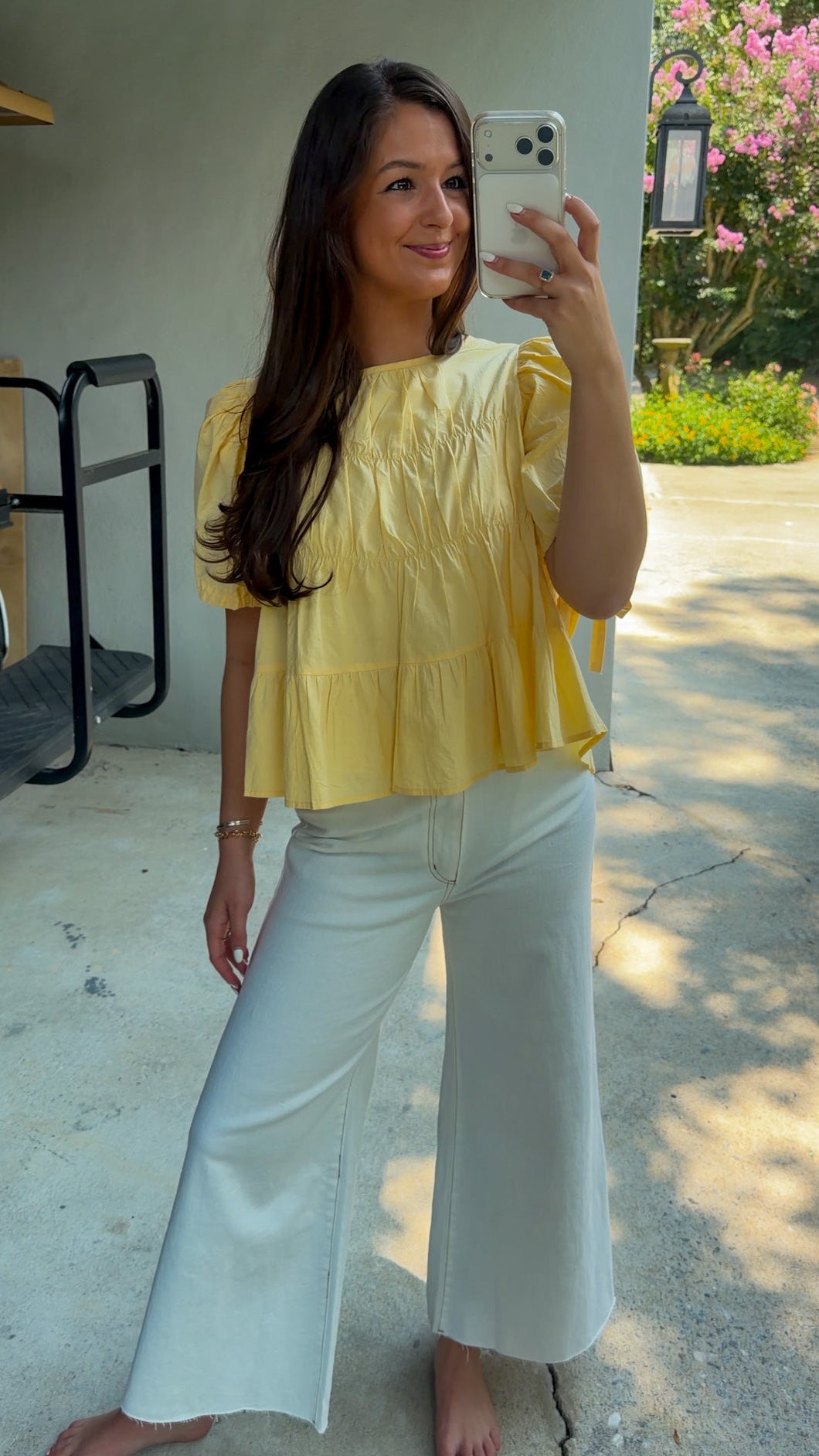 Butter yellow babydoll top featuring a round neckline, tiered shirring, short puff sleeves with adjustable tie cuffs, a ruffle-trimmed back, keyhole button closure, and a relaxed semi-cropped silhouette.