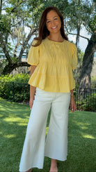 Butter yellow babydoll top featuring a round neckline, tiered shirring, short puff sleeves with adjustable tie cuffs, a ruffle-trimmed back, keyhole button closure, and a relaxed semi-cropped silhouette.