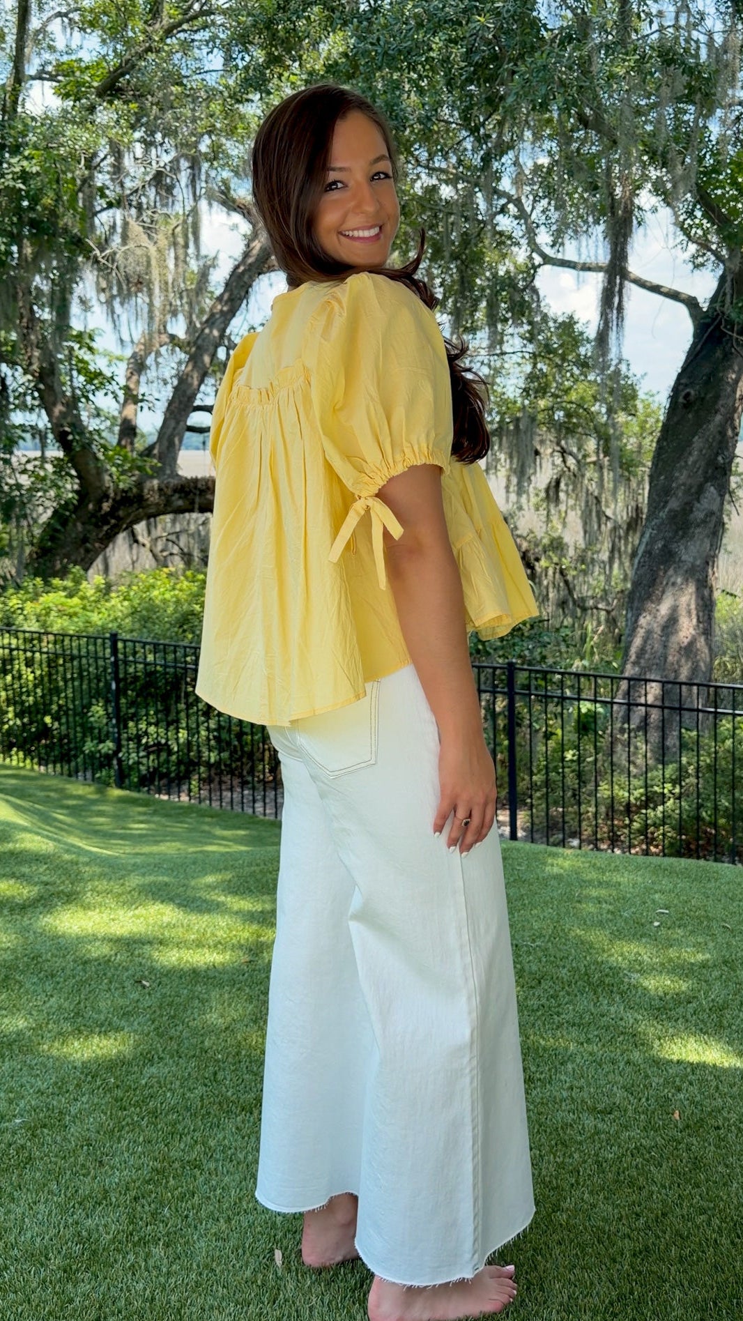 Butter yellow babydoll top featuring a round neckline, tiered shirring, short puff sleeves with adjustable tie cuffs, a ruffle-trimmed back, keyhole button closure, and a relaxed semi-cropped silhouette.