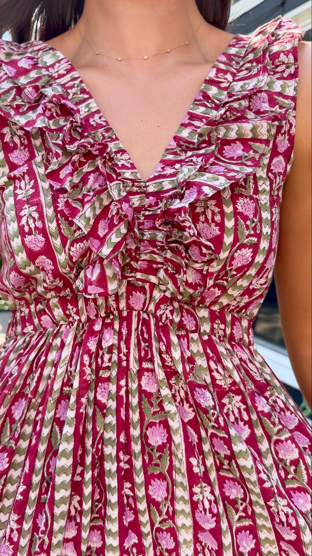Close-up of a sleeveless ruffled dress with a deep V-neck, featuring a pink and olive green floral and striped pattern.